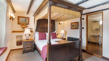 Un lit à baldaquin, des tables de chevet avec des lampes, un tableau encadré au mur et une vue sur la salle de bain.