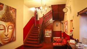 Eine Hotelhalle mit Treppe, einer Rezeption, einer Uhr und einem Buddha-Gemälde.