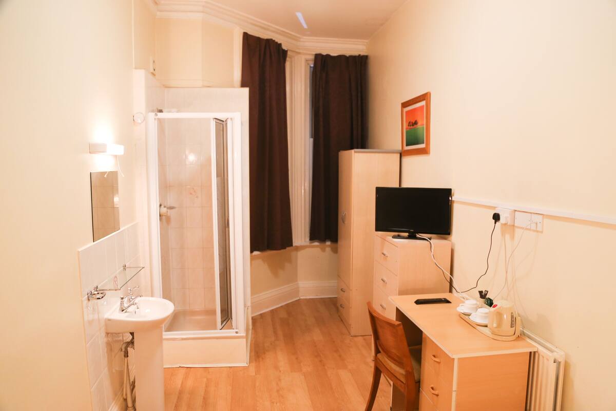 A hotel room with a shower, sink, desk, and a television.