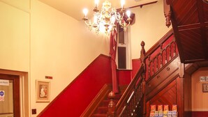 Eine Treppe mit rotem Teppich führt zu einem Raum, der eine Chandelüster, ein rotes Ledersofa und eine Wanduhr beherbergt.