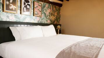 A neatly made bed with white linens in a room with floral wallpaper and wooden beams.