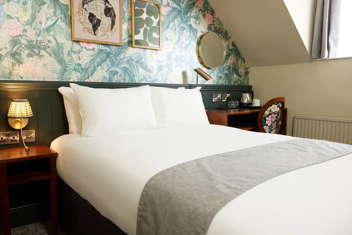 A neatly made bed with white linens, a grey throw, and a wooden nightstand with a lamp.