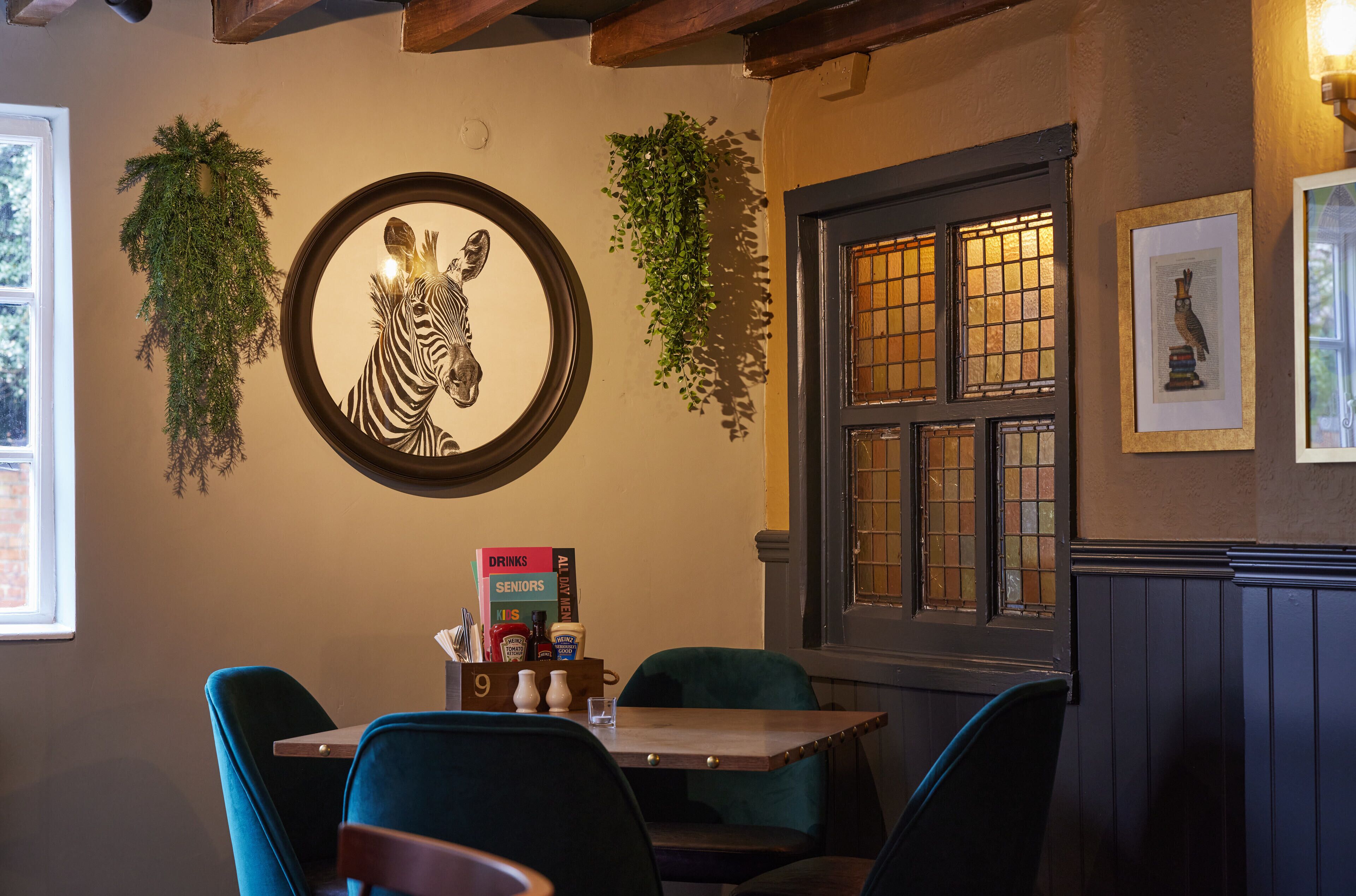 Un interior de restaurante con una mesa de madera, sillas color turquesa, una obra de arte con cebra y un ventanal con vistas.