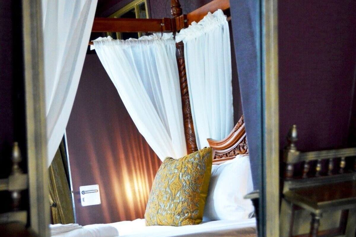 A bedroom with a four-poster bed, white curtains, and a patterned pillow.