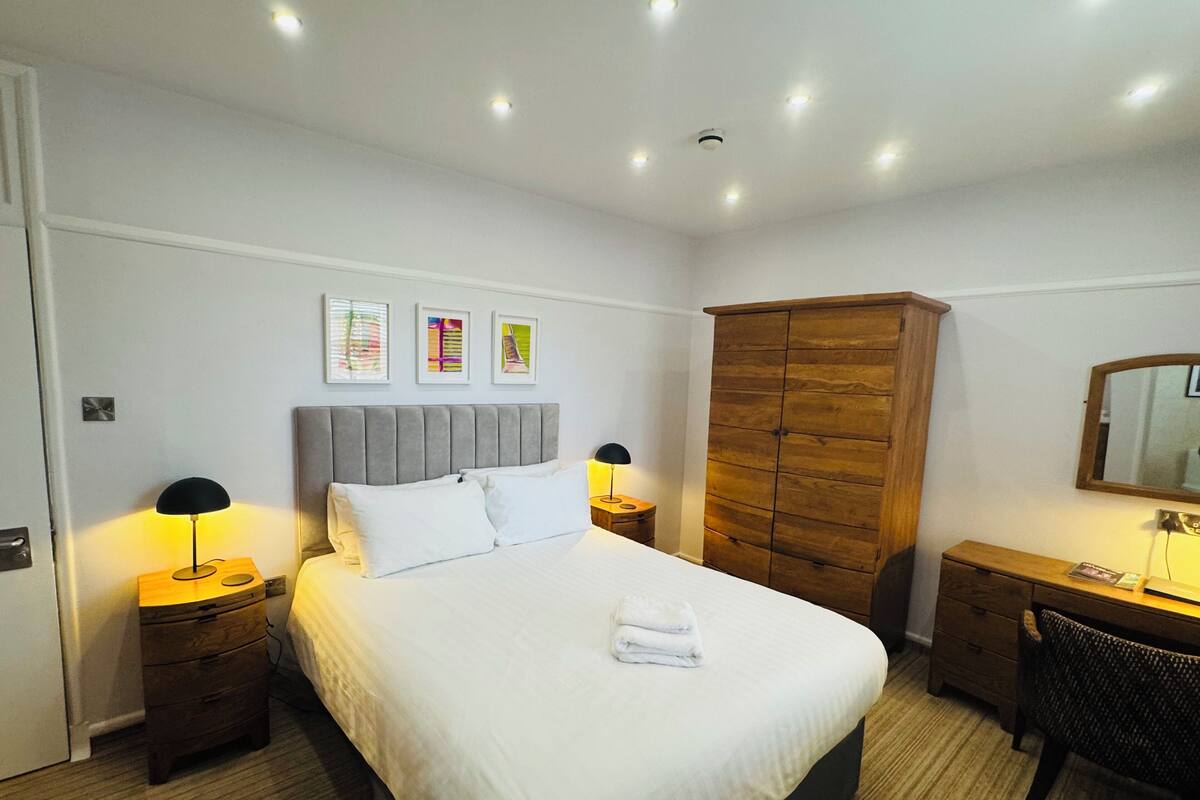 A hotel room with a bed, bedside tables, a wardrobe, a desk, and a mirror.