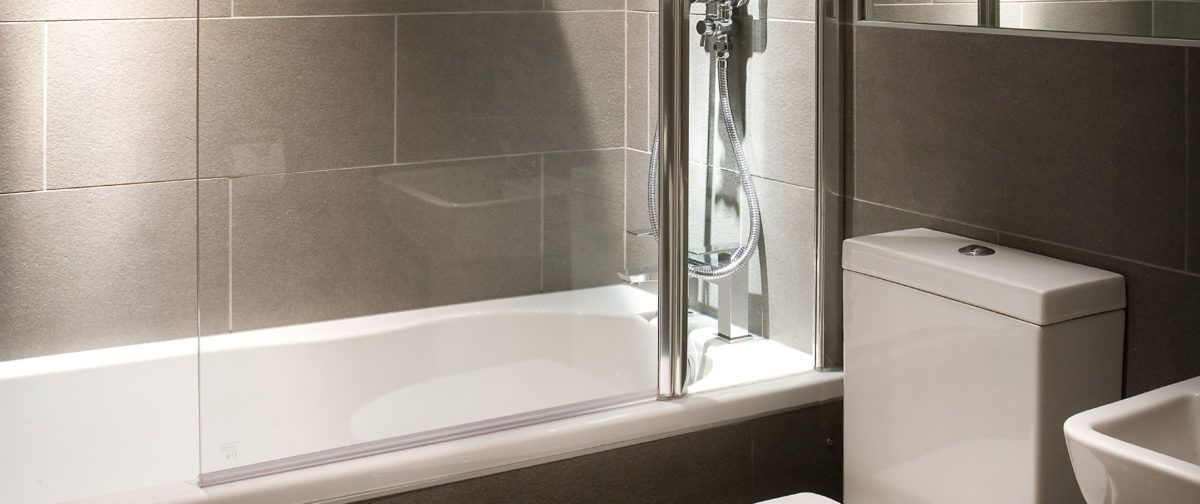 A modern bathroom with a glass-enclosed shower, a white bathtub, and a toilet.
