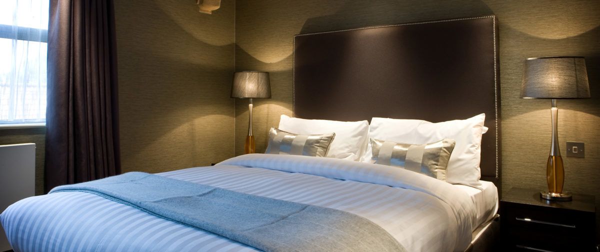 Habitación de hotel con una cama grande, dos mesitas de noche y un ventanal con cortinas.