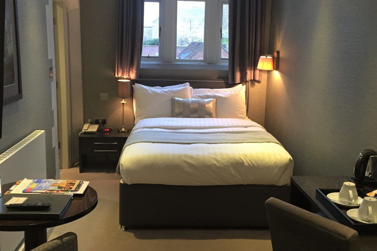 A hotel room with a large bed, bedside tables, a desk with a chair, and a window with curtains.