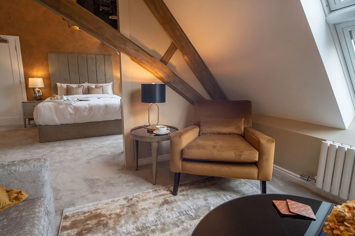 A bedroom with a bed, a chair, a table with a lamp, and a radiator.