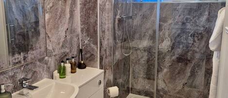 A bathroom with a marble wall, a glass shower enclosure, a white sink, and a toilet.