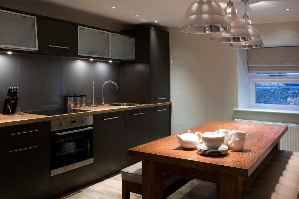 A modern kitchen with dark cabinetry, a wooden dining table, and a window with a city view.
