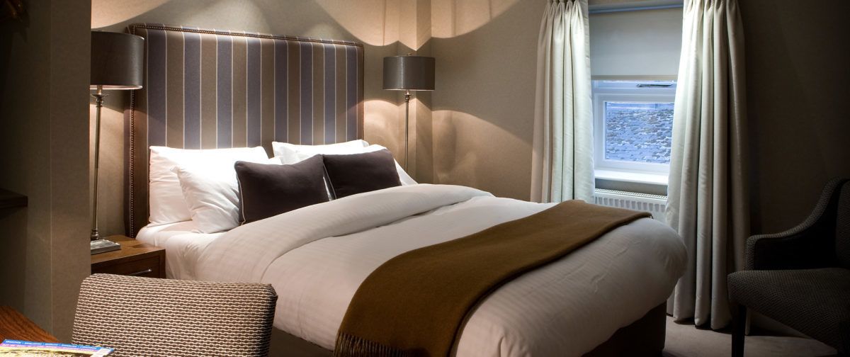 Une chambre d’hôtel avec un grand lit, deux lampes de chevet, une fenêtre avec des rideaux et une chaise.