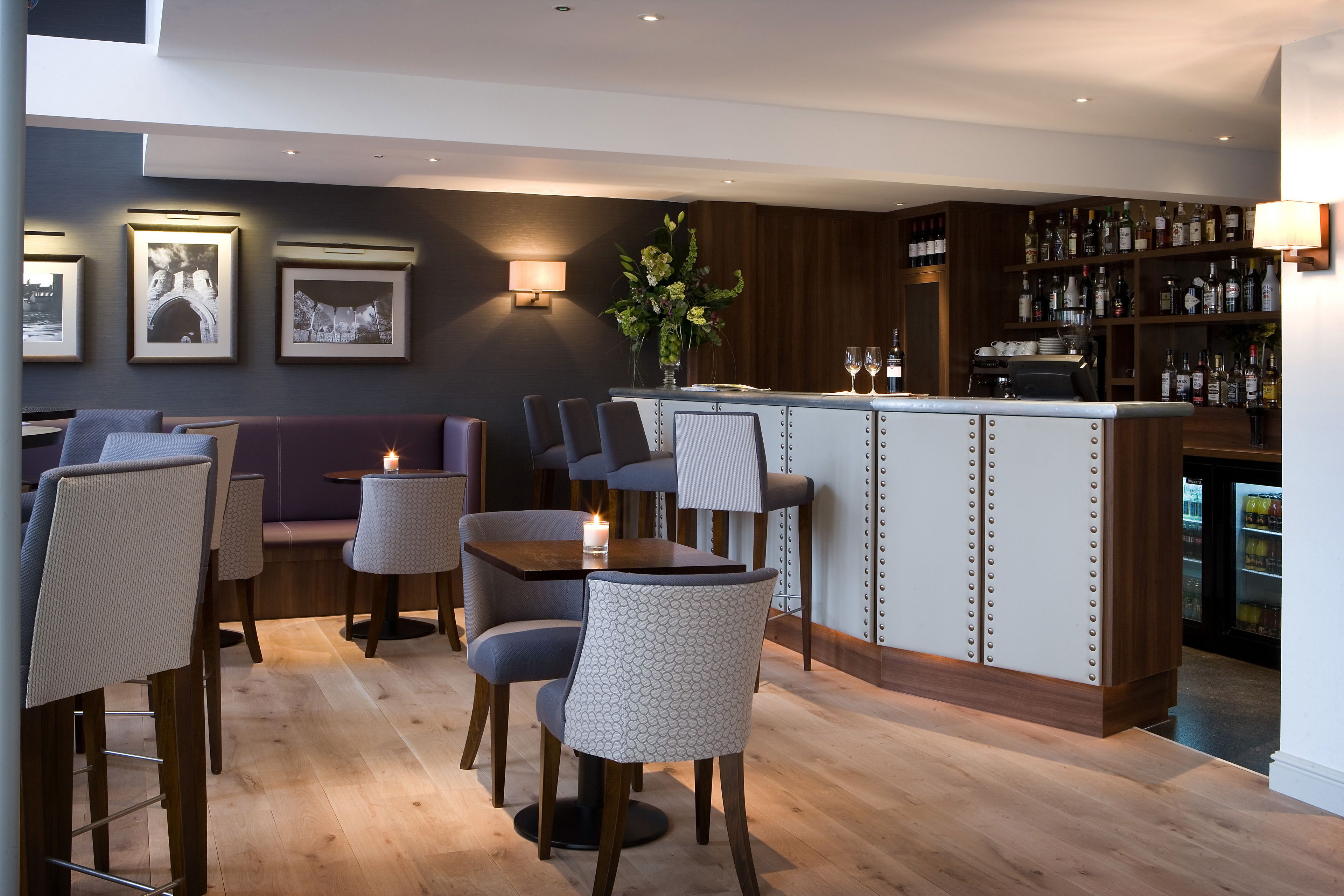 Eine moderne Bar mit Holztresen, Sitzgelegenheiten mit gepolsterten Stühlen und einer Wandleuchte.