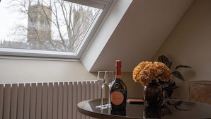 Et værelse med ovenlys, et bord med vin, et vinglas og en vase med blomster.