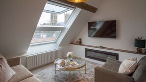 En moderne stue med skråloft, pejs, fladskærms-tv og et bord med blomsterarrangement.