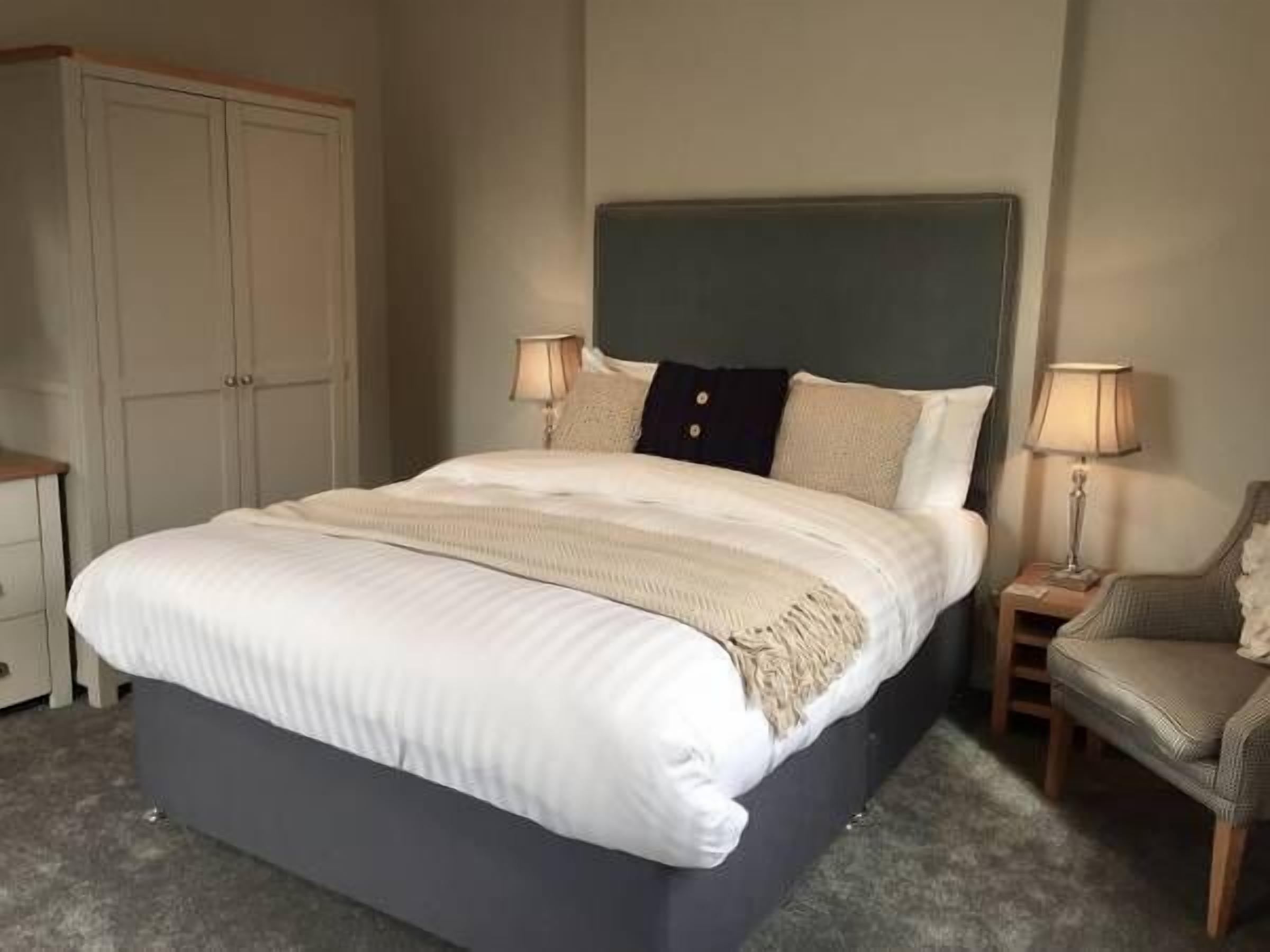 A bedroom with a large bed, a wardrobe, two bedside lamps, and a chair.