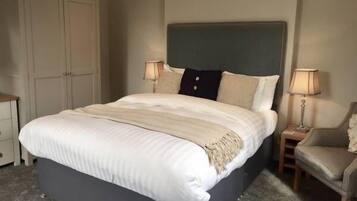 A bedroom with a large bed, a wardrobe, two bedside lamps, and a chair.