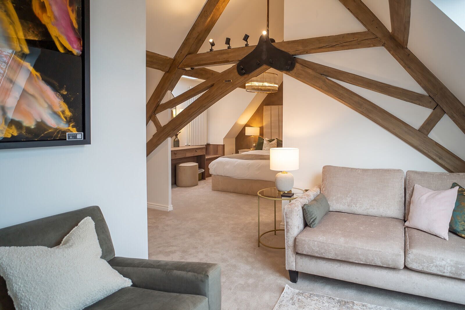 A cozy loft bedroom with exposed wooden beams, a bed, a nightstand, and a lamp.