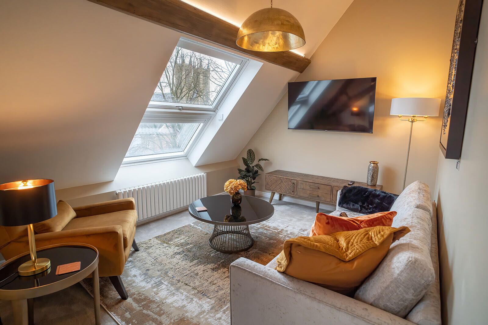 Una sala de estar moderna con techo inclinado, una mesa de centro redonda, un sofá y un televisor montado en la pared.