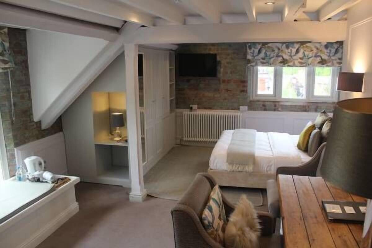 A bedroom with a bed, a desk, a chair, a lamp, and a window.