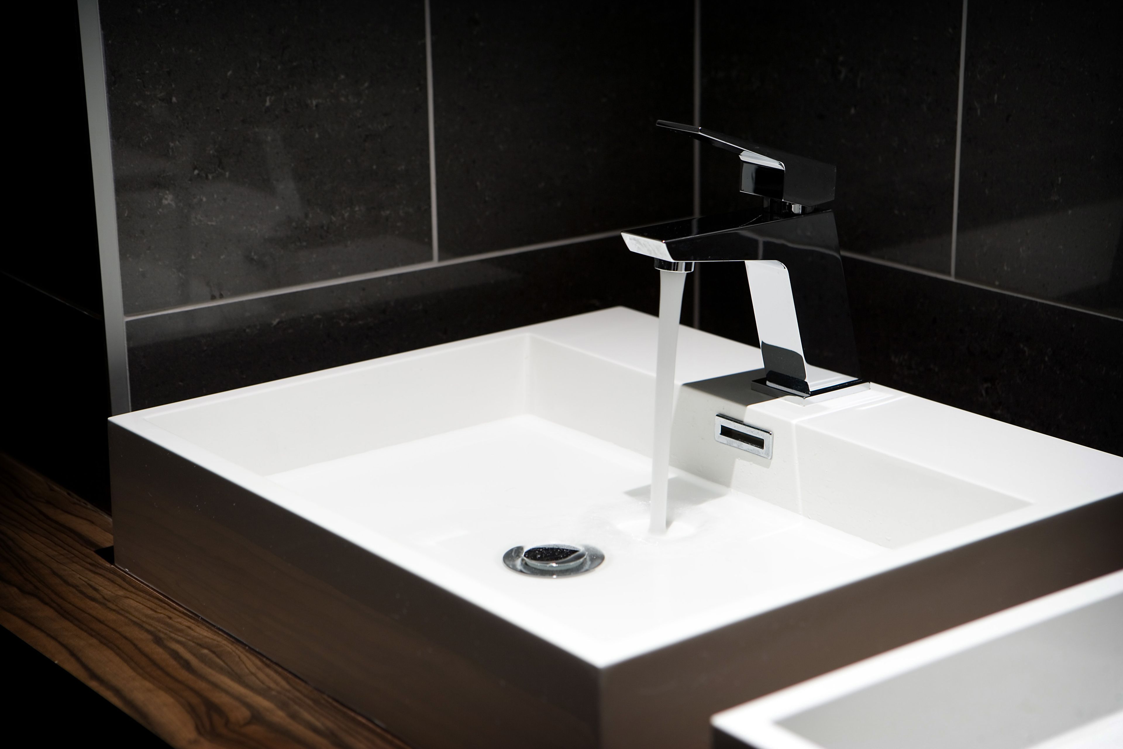 A modern bathroom with a white sink, a chrome faucet, and a wooden floor.