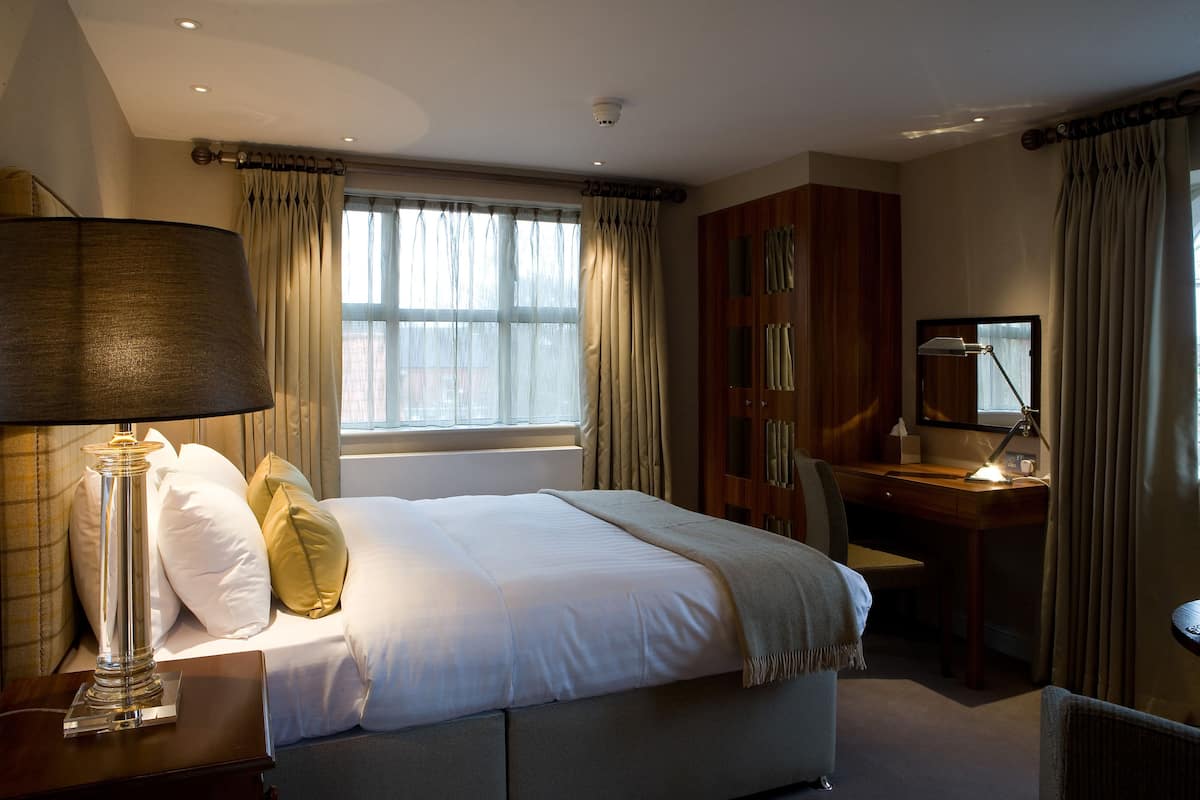 A hotel room with a bed, a desk, a lamp, and curtains.