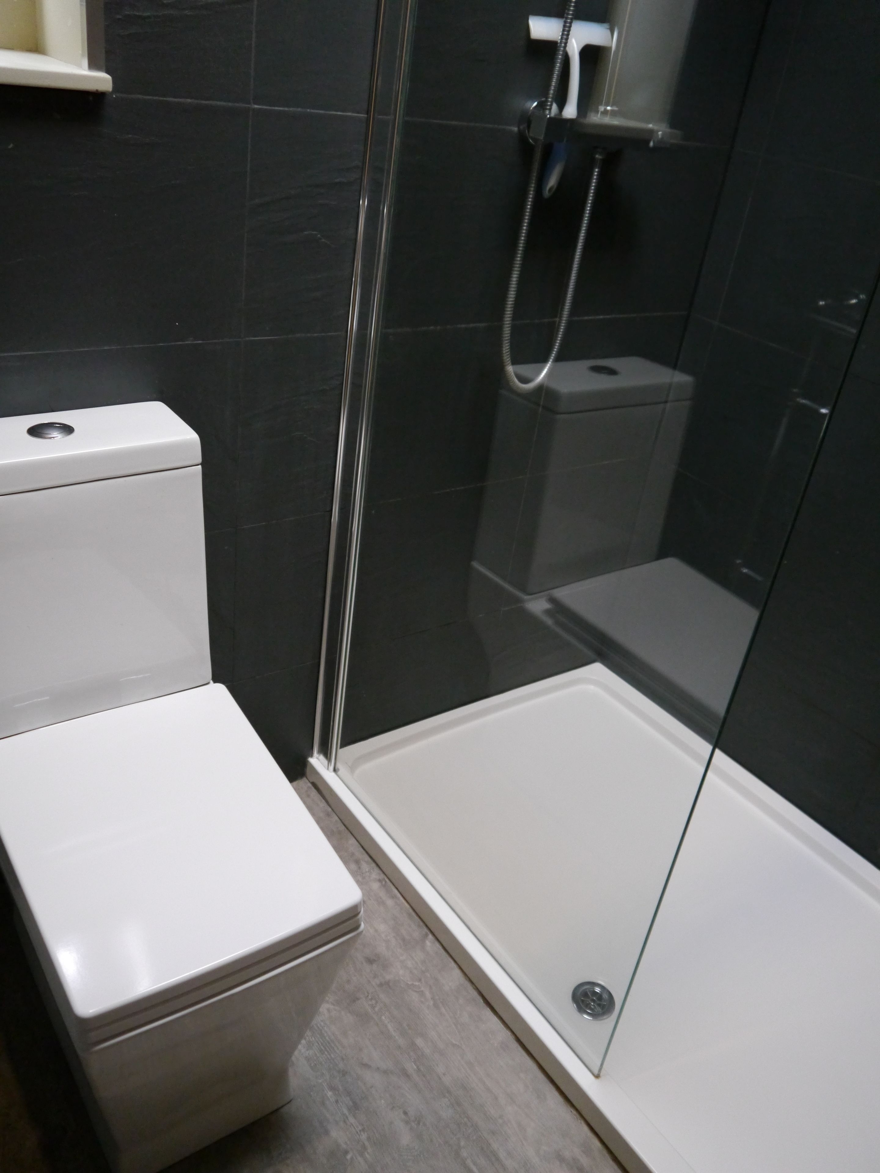 Une salle de bain moderne avec une douche à parois de verre, des toilettes blanches et un mur recouvert de carreaux foncés.