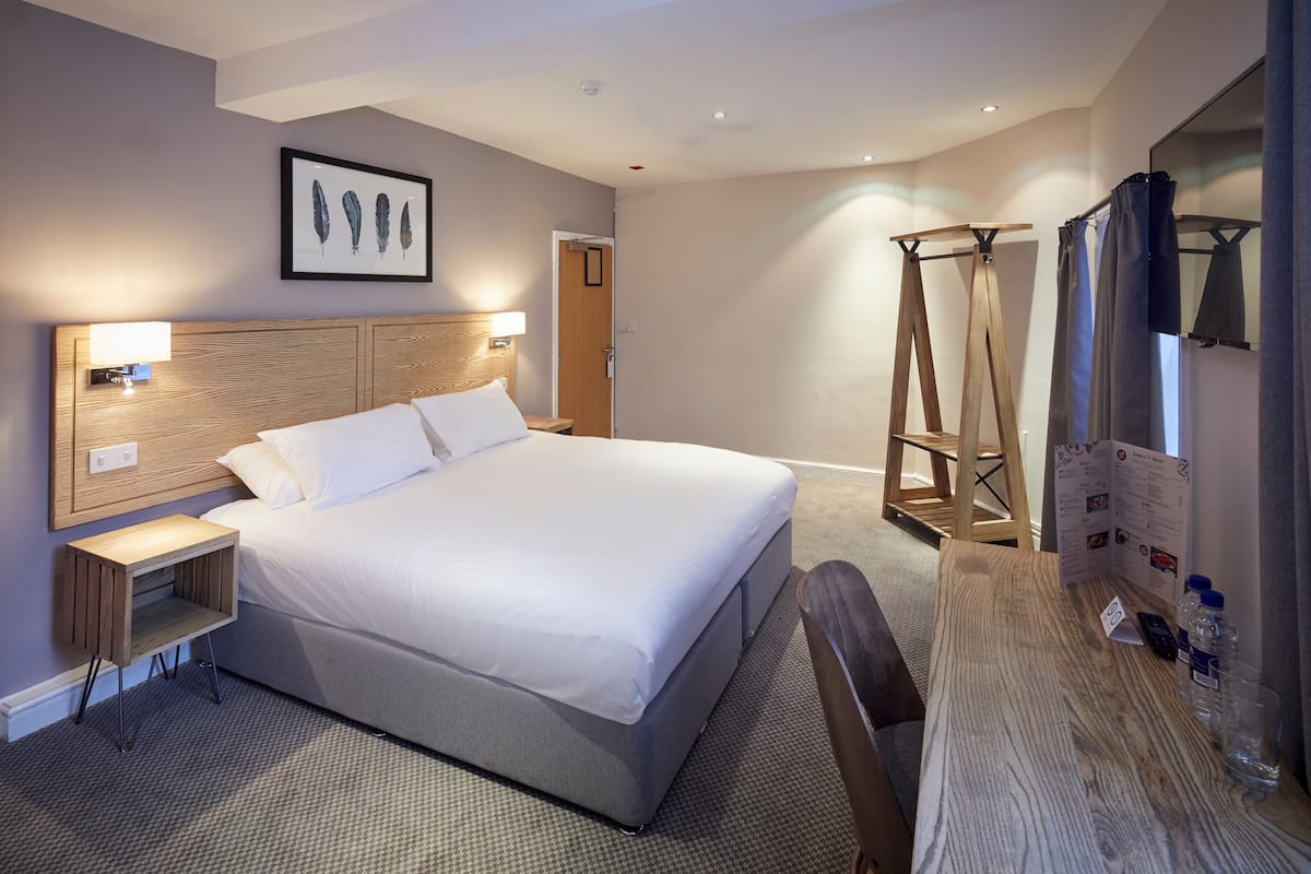 A hotel room with a large bed, wooden headboard, bedside tables with lamps, a wooden desk, and a shower area.