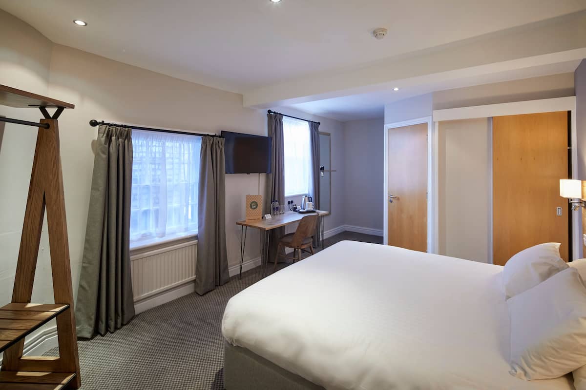 A hotel room with a large bed, a desk with a chair, a television, and a wardrobe.