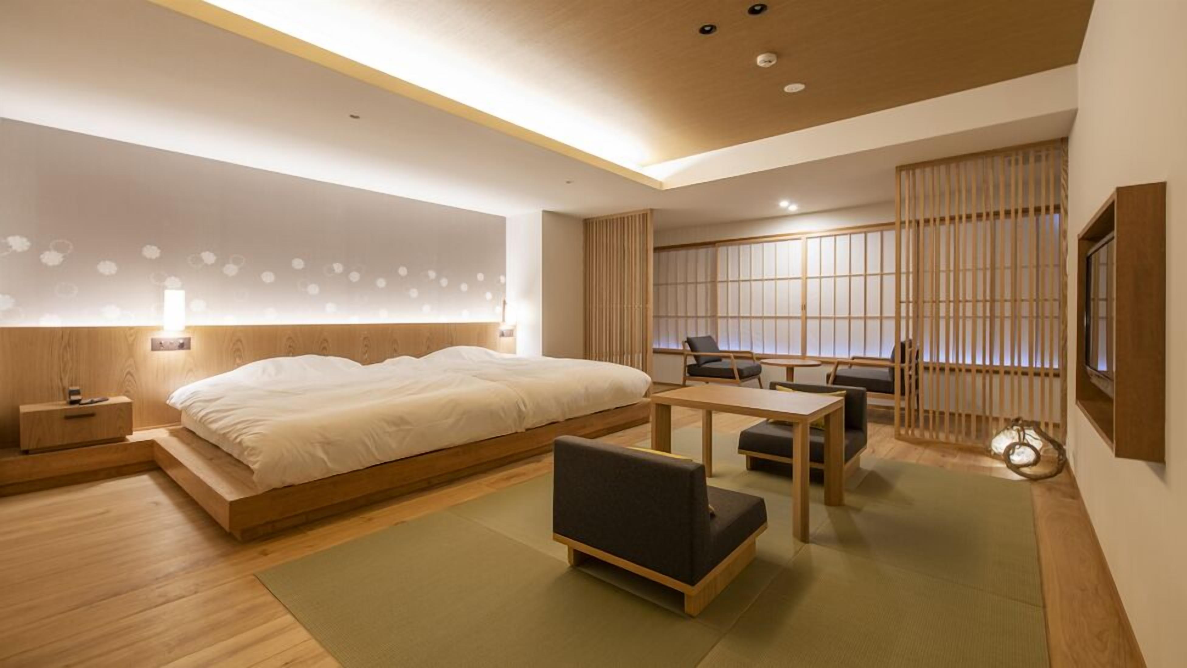 Een moderne hotelkamer met een groot bed, een klein bureau, een stoel en uitzicht op een traditionele Japanse kamer.
