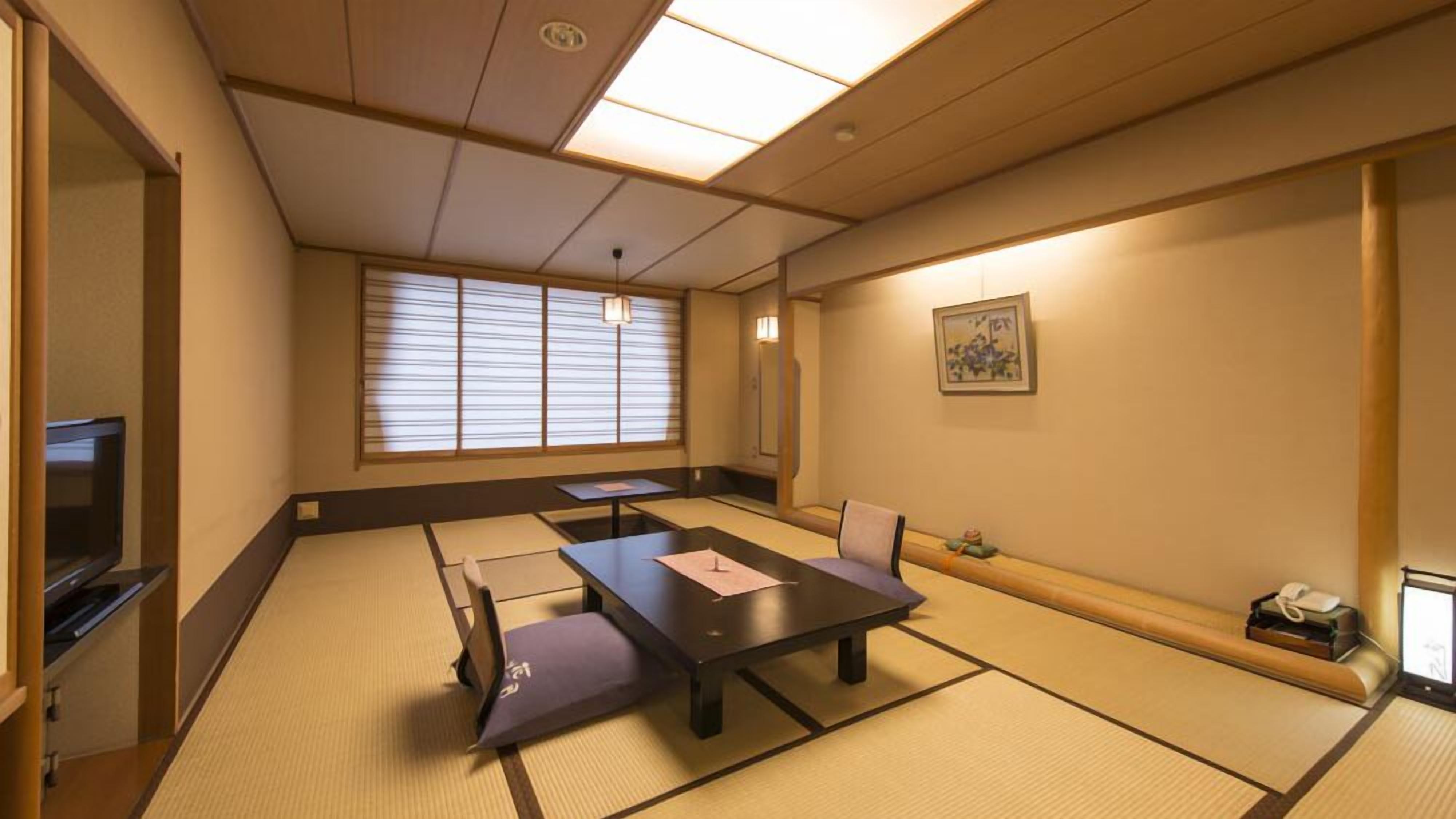 Een traditionele Japanse kamer met tatami vloerbedekking, een lage tafel, een bank, een televisietoestel en een schilderij aan de muur.