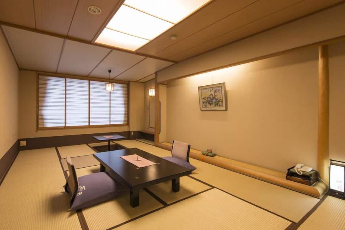 Een traditionele Japanse kamer met tatami vloerbedekking, een lage tafel, een bank, een televisietoestel en een schilderij aan de muur.