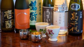 Variedad de botellas de sake y tazas tradicionales de té japonesas sobre una mesa de madera.