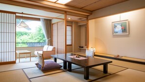 Une pièce de style japonais traditionnel, avec un sol recouvert de tatamis, une table basse, un fauteuil rembourré et des portes coulissantes donnant sur un balcon avec vue sur la verdure.