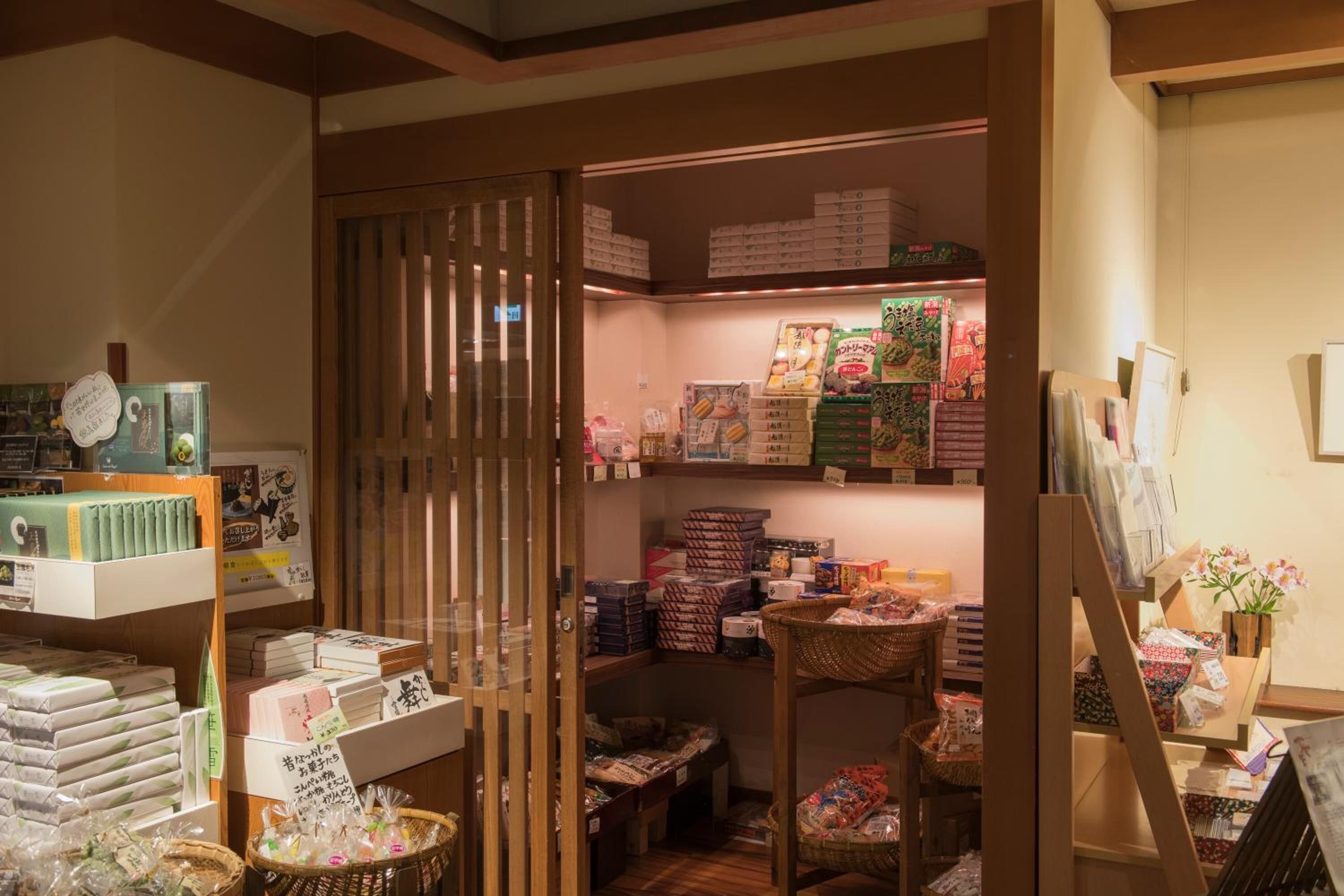 A cozy, well-organized store with shelves stocked with various packaged goods, baskets, and a display of books and magazines.