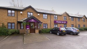 A brick building with a sign for Premier Inn, two cars parked in front, and a paved entrance area. - Premier Inn Liverpool Rainhill (Liverpool)