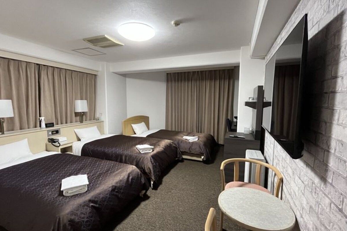 A hotel room with two beds, a TV, a desk, and a chair.