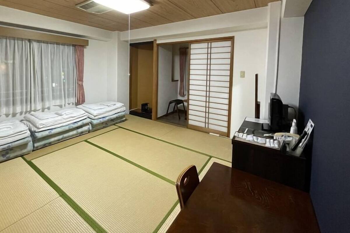 A tatami mat room with a futon bed, a wooden table, and a sliding door.
