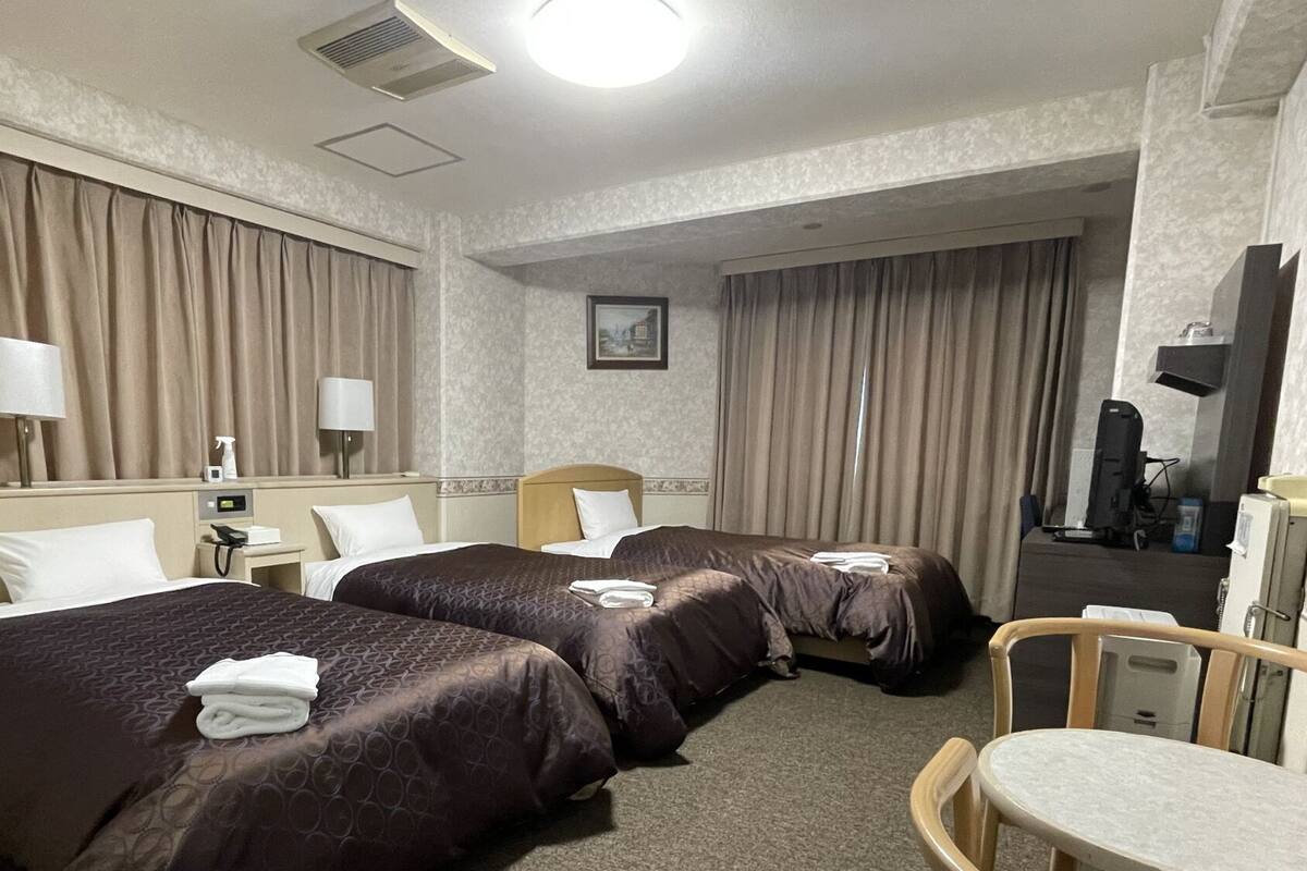 A hotel room with two beds, a desk, a chair, a TV, and a bathroom.