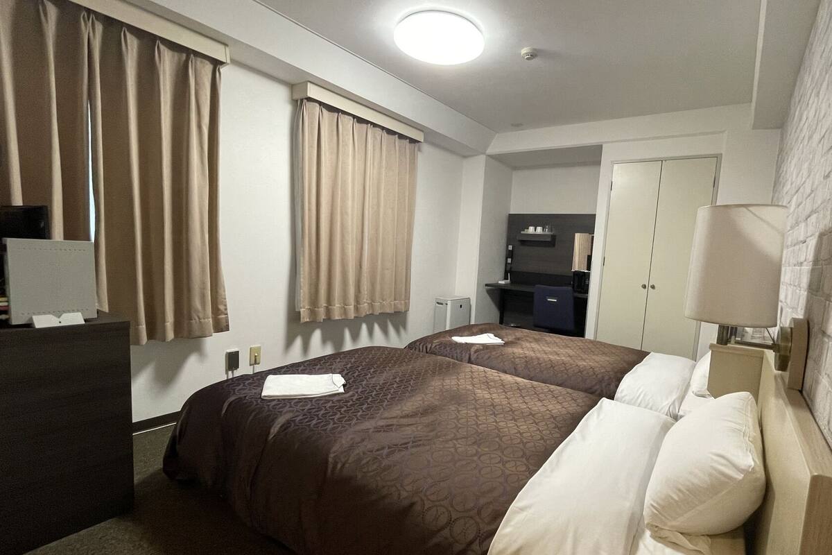A hotel room with two beds, a desk, a wardrobe, and a mirror.