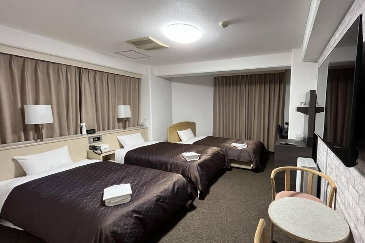 A hotel room with two beds, a TV, a desk, and a chair.
