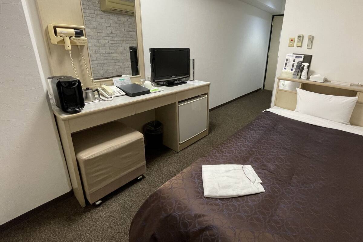 A hotel room with a bed, a desk with a computer, a telephone, and a small trash bin.