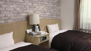 A hotel room with a brick-patterned wall, a bed with a dark brown bedspread, a bedside table with a lamp, a phone, and a small box. - Crystal Hiroshima (Hiroshima)