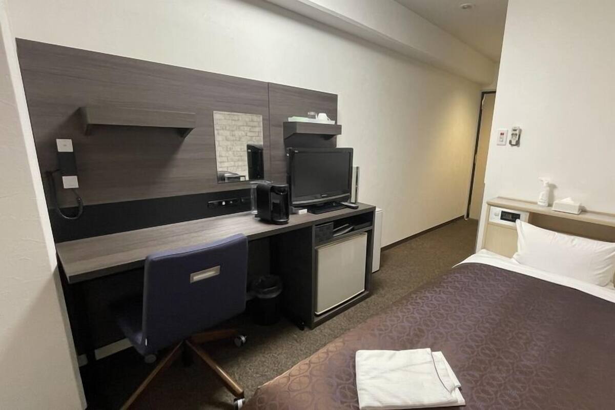 A hotel room with a bed, a desk with a computer, a small TV, and a coffee maker.