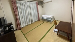 A room with tatami flooring, a bed with a mattress, a TV on a stand, and an air conditioning unit. - Crystal Hiroshima (Hiroshima)