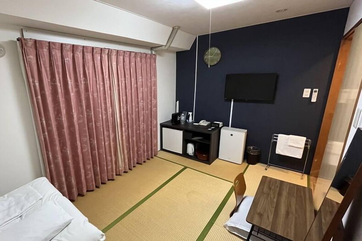 A hotel room with a bed, a desk with a computer, a TV, and a small table.