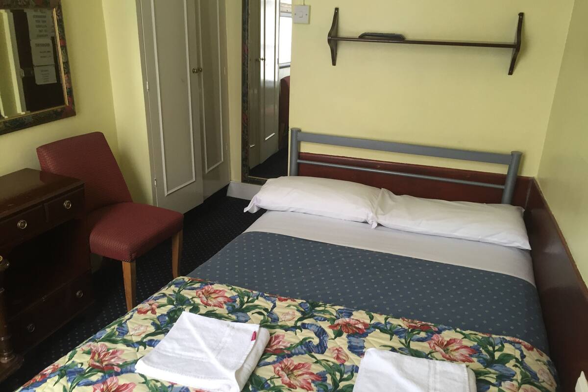 A hotel room with a bed, a chair, a desk, and a wardrobe.