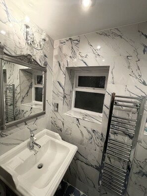 A bathroom with a marble backsplash, a sink, a mirror, and a towel rack.