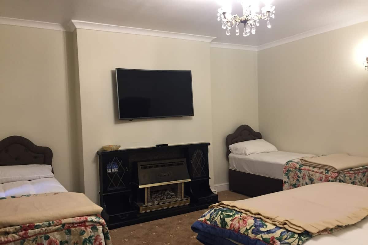 A hotel room with two beds, a flat-screen TV, a fireplace, and a chandelier.
