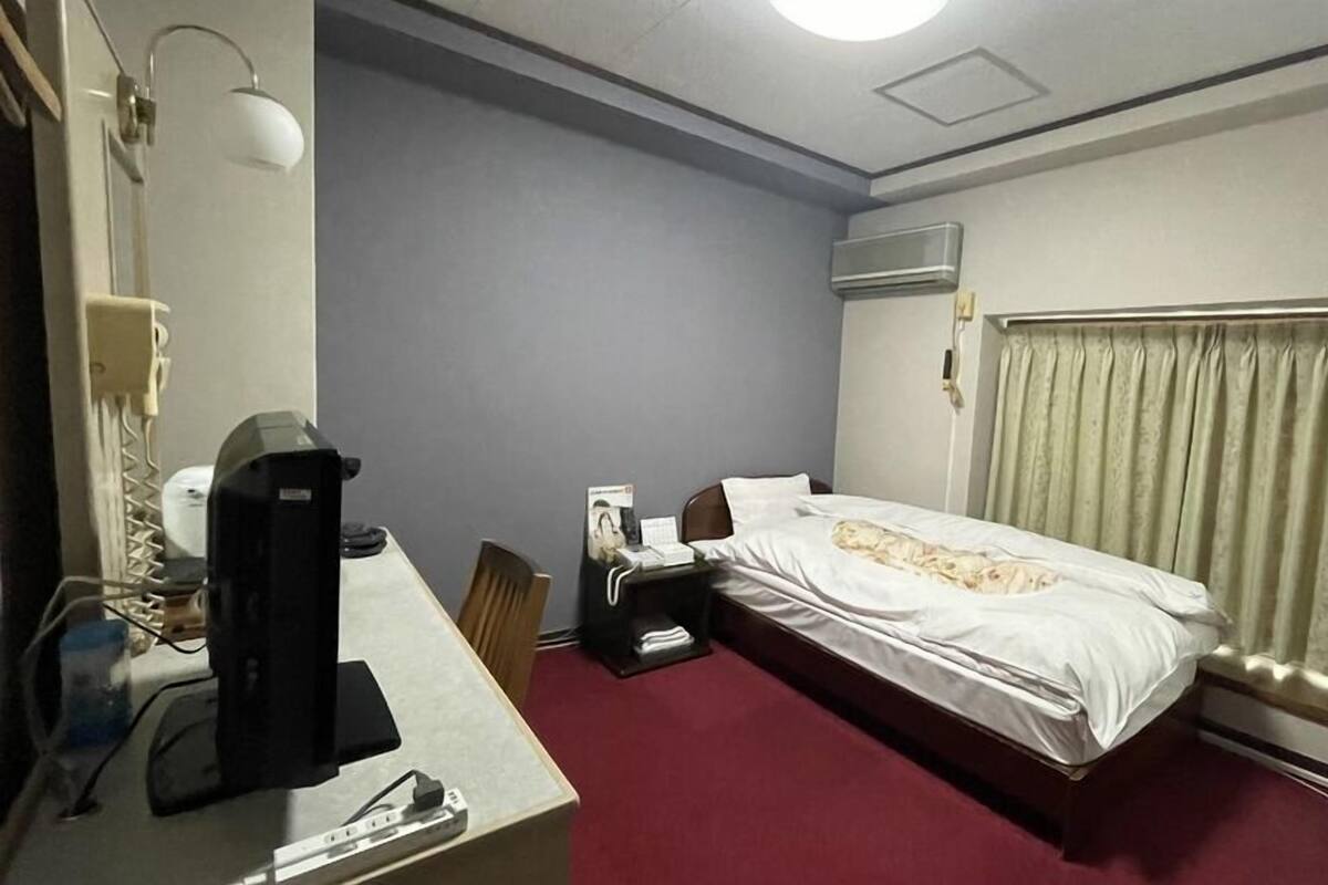 A hotel room with a bed, desk, chair, and a telephone.